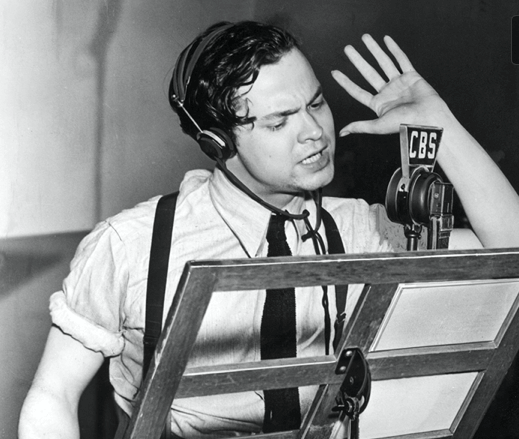 Orson Welles acting for radio with hand raised in front of microphone